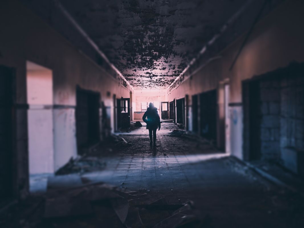 A photo of a person walking down the hallway of a deserted and seemingly-abandoned building. Photo by Andrew Amistad on Unsplash.