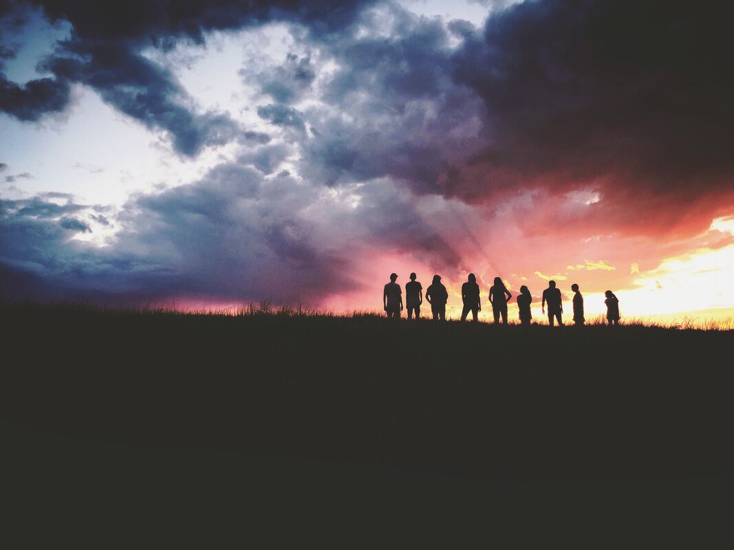 photo of 9 people in silhouette against a multicolored sunset