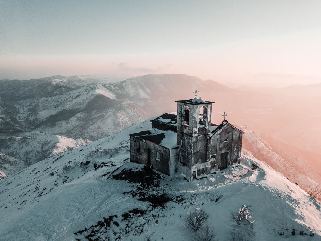 a photo of a seemingly-abandoned church on the top of a snowy mountain, with a hazy sky